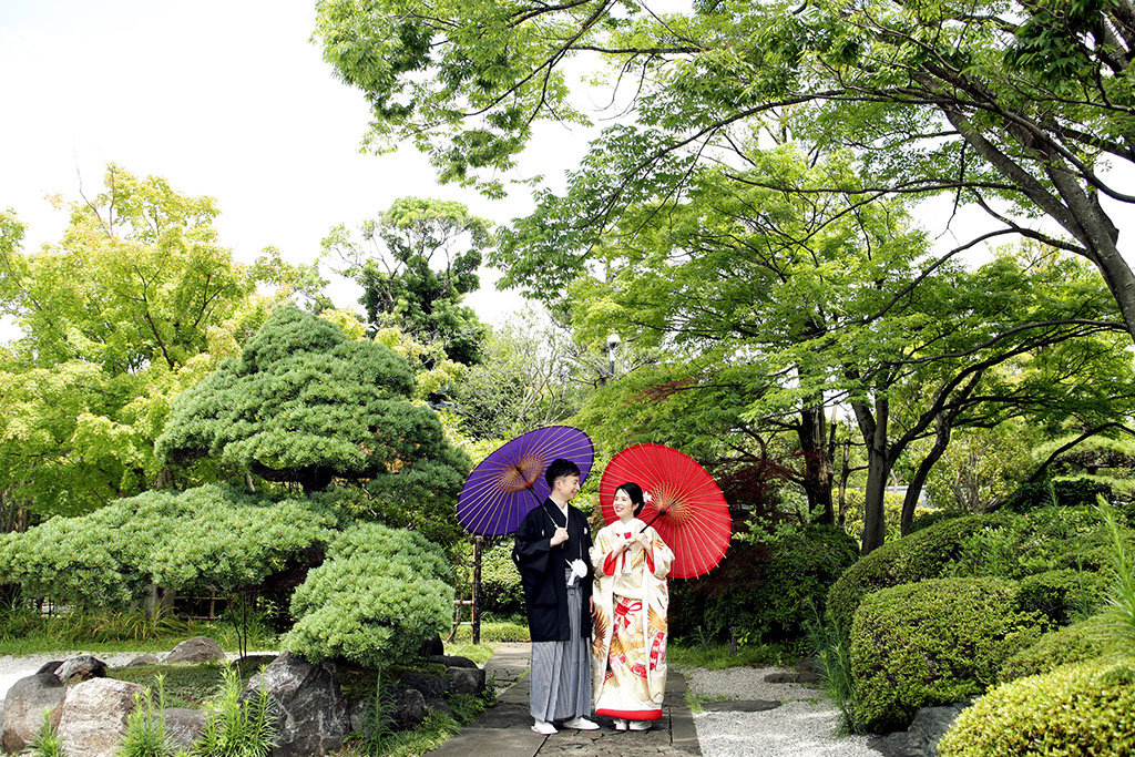 池のほとりの浮見堂でカメラを向きポーズをとる新郎新婦